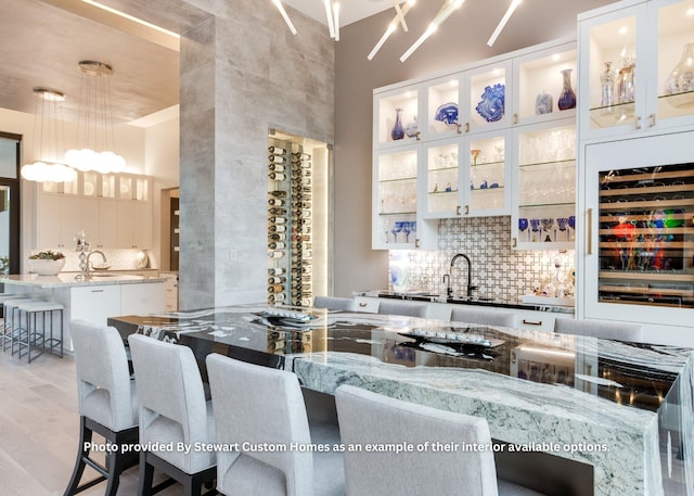 kitchen featuring light wood finished floors, a kitchen island with sink, a sink, decorative backsplash, and a kitchen bar