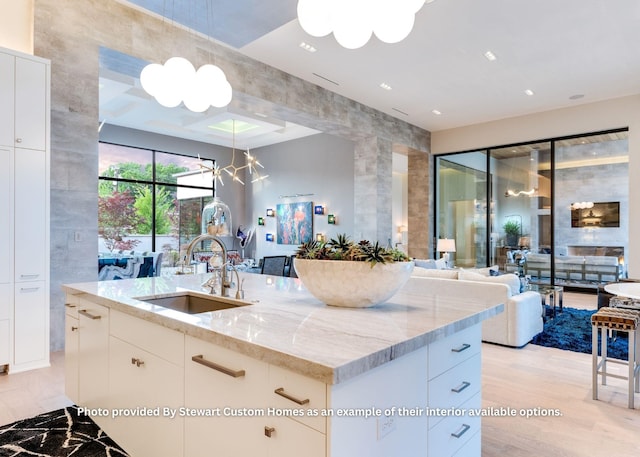 kitchen featuring a kitchen island with sink, a sink, light stone counters, open floor plan, and a chandelier