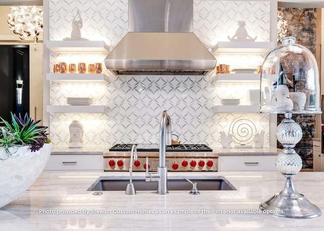 kitchen with open shelves, wall chimney exhaust hood, light stone countertops, and a sink