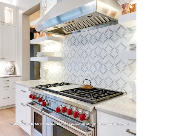 kitchen featuring wall chimney range hood, decorative backsplash, high end stainless steel range oven, white cabinetry, and open shelves