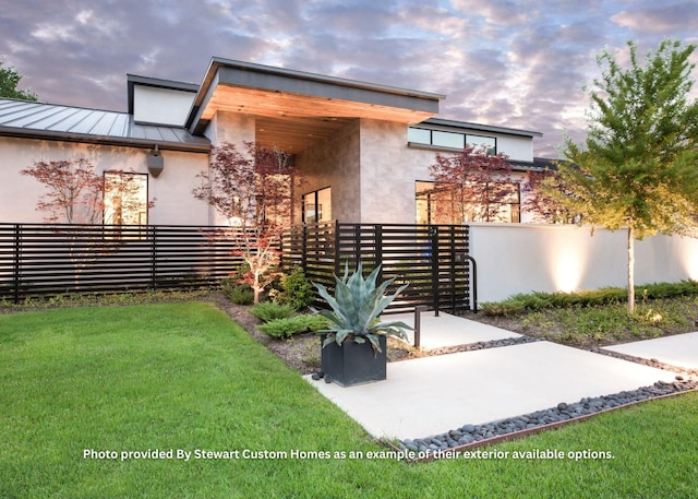 exterior space featuring stucco siding, a standing seam roof, fence, a yard, and metal roof