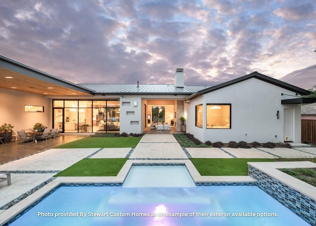 rear view of house featuring stucco siding, a standing seam roof, an outdoor pool, metal roof, and a patio area