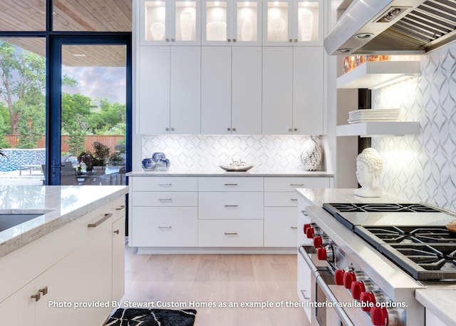 kitchen with tasteful backsplash, light stone countertops, range hood, high end stainless steel range oven, and white cabinets