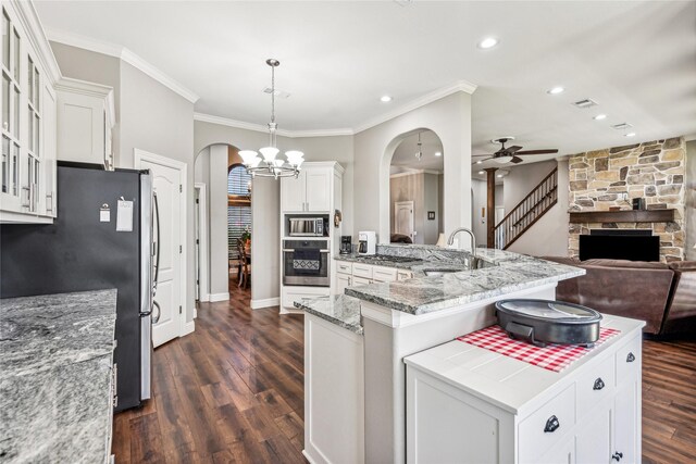 kitchen featuring ceiling fan with notable chandelier, a sink, stainless steel appliances, arched walkways, and a fireplace