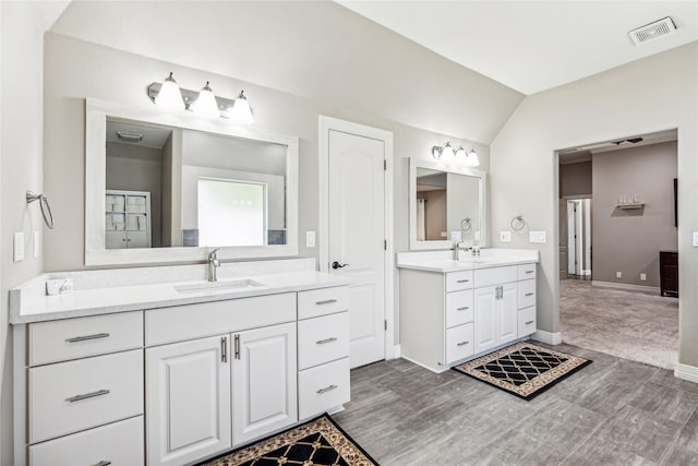 full bath featuring visible vents, two vanities, lofted ceiling, and a sink