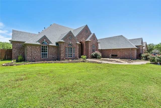 view of front of property featuring brick siding, roof with shingles, a front lawn, and fence
