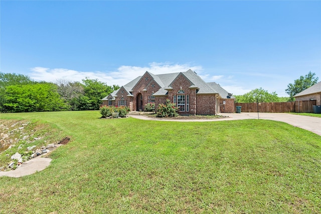 view of front facade featuring a front yard, brick siding, driveway, and fence