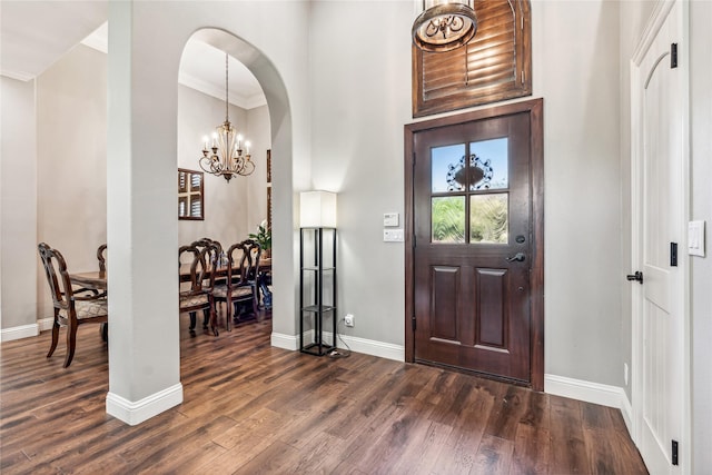 foyer entrance featuring crown molding, baseboards, dark wood-type flooring, an inviting chandelier, and arched walkways
