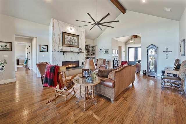 living area featuring beamed ceiling, a ceiling fan, wood finished floors, and a fireplace