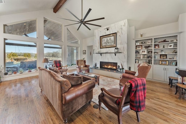 living area with a high end fireplace, beam ceiling, light wood-style flooring, and ceiling fan