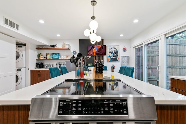 kitchen featuring brown cabinetry, visible vents, light countertops, stacked washer and dryer, and range with electric stovetop