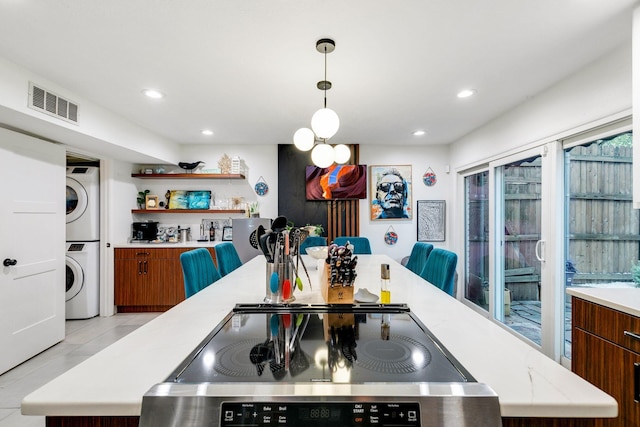 kitchen featuring visible vents, stacked washer and clothes dryer, brown cabinetry, light countertops, and stove