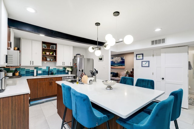 kitchen featuring a sink, open shelves, stainless steel fridge, and a kitchen bar