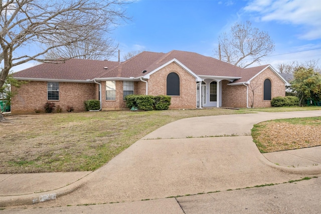 ranch-style home with brick siding, roof with shingles, a front yard, and curved driveway