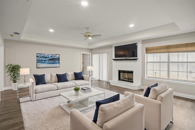 living area featuring a ceiling fan, wood finished floors, and a raised ceiling