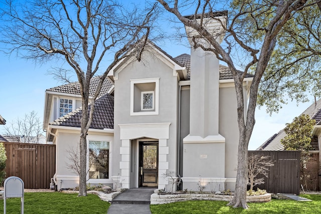 view of front of home with a front lawn, stucco siding, a tiled roof, and fence