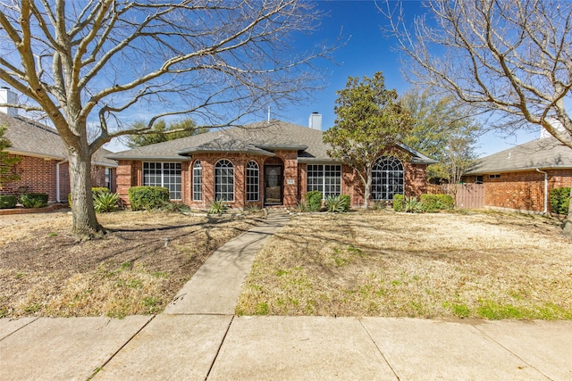ranch-style house with a shingled roof, fence, brick siding, and a chimney