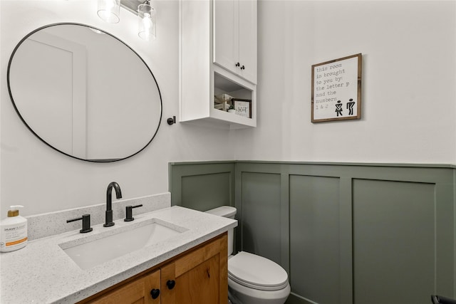 bathroom with vanity, a decorative wall, toilet, and wainscoting