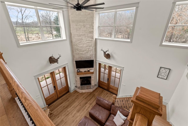 living room with french doors, a stone fireplace, wood finished floors, and a ceiling fan