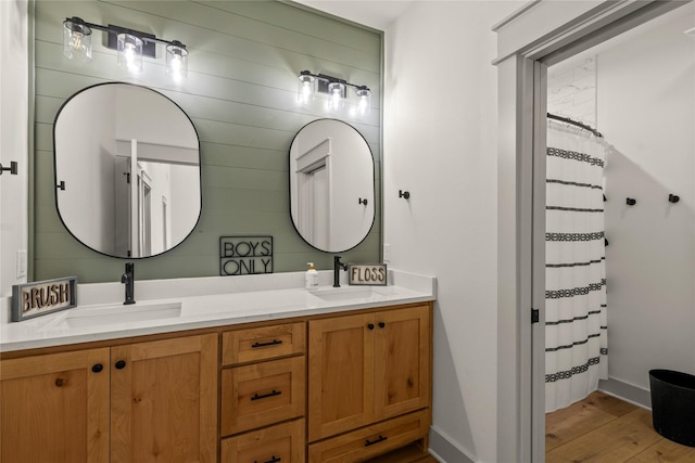 bathroom featuring double vanity, wood finished floors, baseboards, and a sink