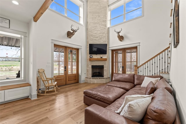 living room with light wood finished floors, beam ceiling, a high ceiling, a fireplace, and french doors