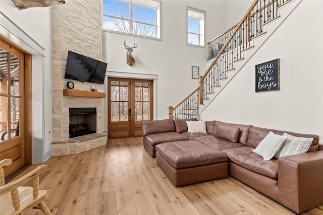 living area featuring a wealth of natural light, a stone fireplace, light wood-style flooring, and a towering ceiling