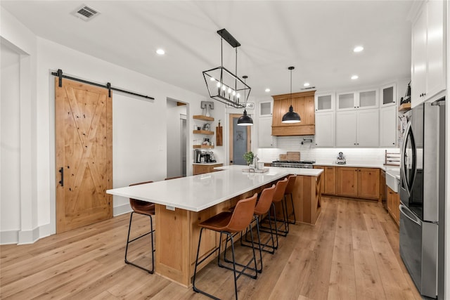 kitchen with visible vents, light wood-style flooring, stainless steel appliances, a barn door, and tasteful backsplash