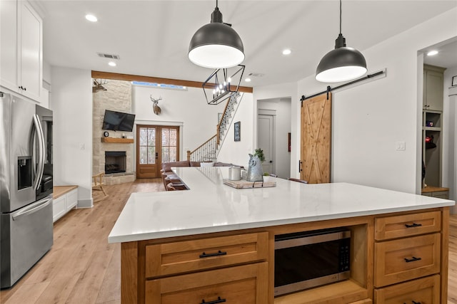 kitchen featuring light wood-style flooring, open floor plan, a barn door, appliances with stainless steel finishes, and a fireplace