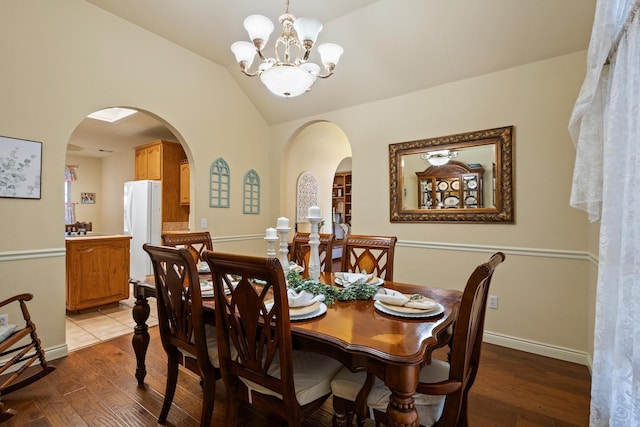 dining space featuring baseboards, lofted ceiling, wood finished floors, arched walkways, and a notable chandelier