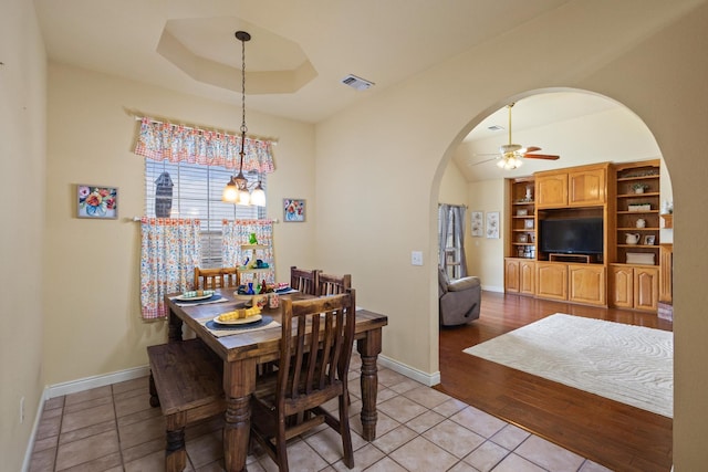 dining space featuring visible vents, baseboards, arched walkways, a raised ceiling, and ceiling fan with notable chandelier
