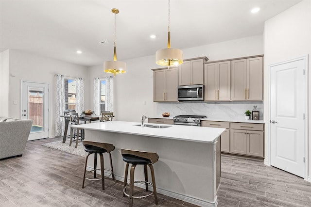 kitchen featuring gray cabinetry, a breakfast bar area, decorative backsplash, stainless steel appliances, and a sink