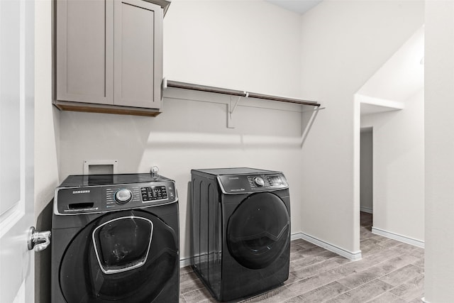 laundry room featuring cabinet space, light wood-style floors, baseboards, and washing machine and clothes dryer