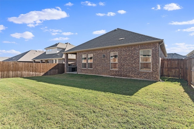 rear view of property featuring brick siding, a lawn, a fenced backyard, and roof with shingles