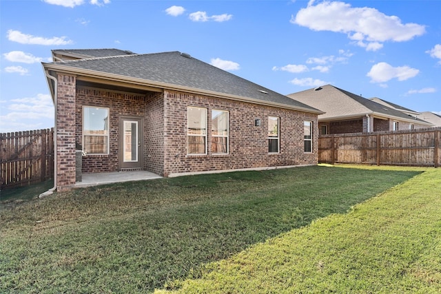 back of house with brick siding, roof with shingles, a fenced backyard, a yard, and a patio