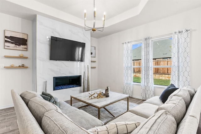 living room featuring a chandelier, a high end fireplace, a tray ceiling, and wood finished floors