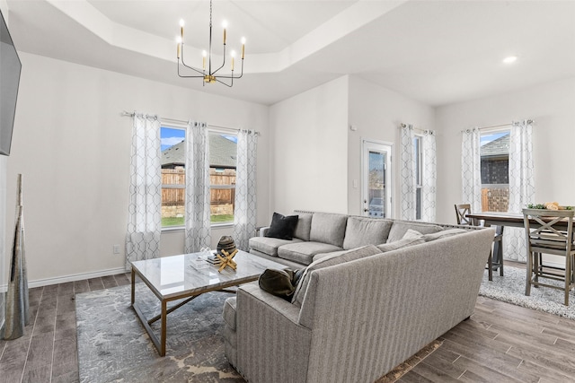 living area with a tray ceiling, wood finished floors, recessed lighting, an inviting chandelier, and baseboards