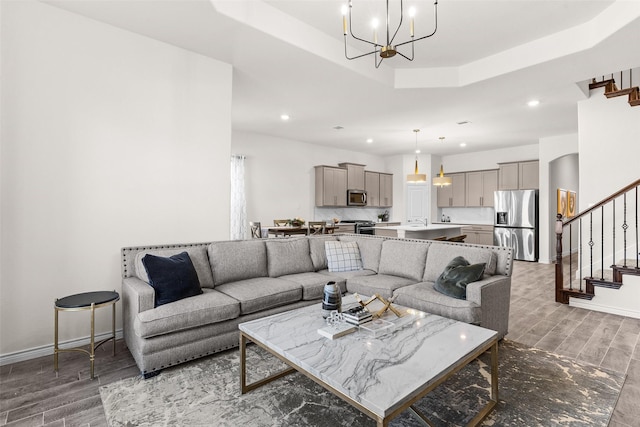 living room featuring stairway, wood finished floors, an inviting chandelier, a tray ceiling, and recessed lighting