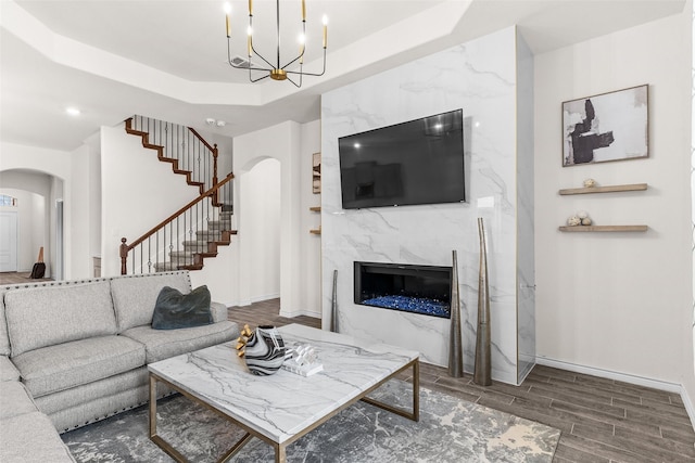 living area featuring wood tiled floor, stairway, a tray ceiling, an inviting chandelier, and arched walkways