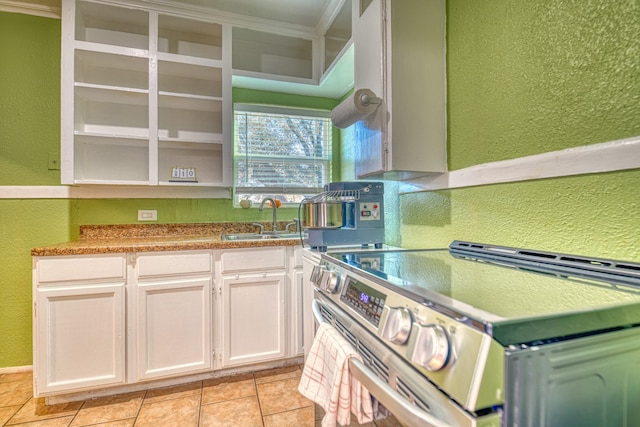 kitchen with stainless steel electric range, a textured wall, light tile patterned flooring, white cabinetry, and a sink