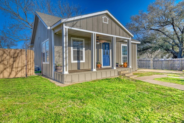 view of front of home with a front lawn, fence, covered porch, board and batten siding, and ceiling fan
