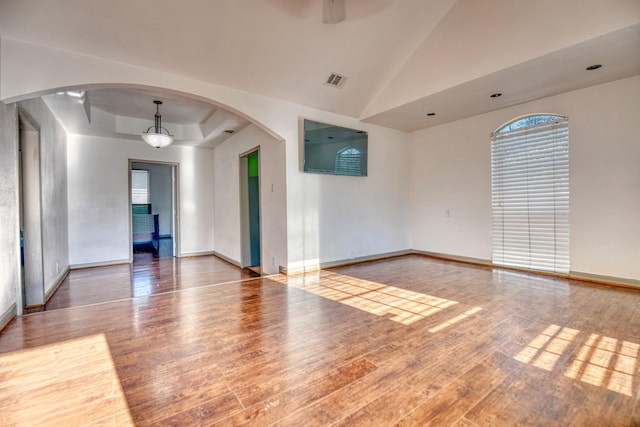 unfurnished room with wood finished floors, baseboards, a tray ceiling, arched walkways, and ceiling fan