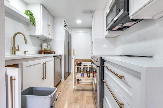 kitchen featuring visible vents, appliances with stainless steel finishes, light wood-type flooring, a sink, and white cabinets