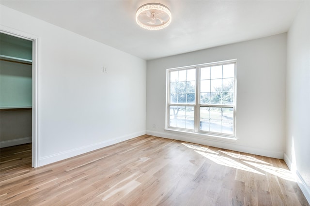 unfurnished bedroom featuring baseboards, a spacious closet, light wood finished floors, and a closet