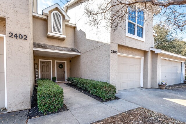 view of exterior entry with a garage, stucco siding, and driveway
