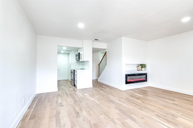 unfurnished living room with light wood-style floors, baseboards, visible vents, and stairway