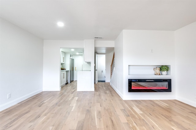 unfurnished living room with visible vents, light wood-type flooring, baseboards, a glass covered fireplace, and recessed lighting