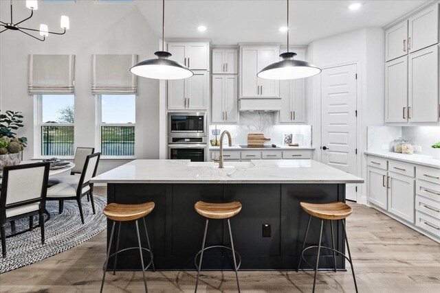 1210 Terrain Ln, Midlothian, TX 76065 - kitchen featuring stainless steel appliances, decorative backsplash, light wood-style floors, a kitchen island with sink, and a kitchen bar