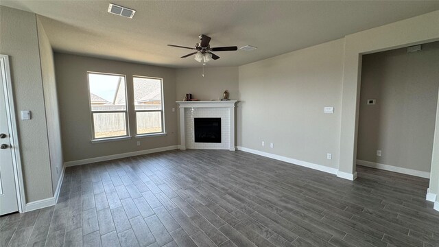 unfurnished living room with a brick fireplace, dark wood-style floors, visible vents, and ceiling fan