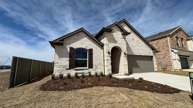 french country home featuring stone siding, an attached garage, concrete driveway, and fence
