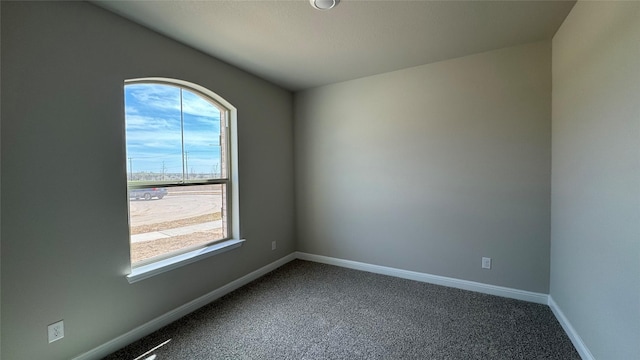 spare room featuring baseboards and dark colored carpet